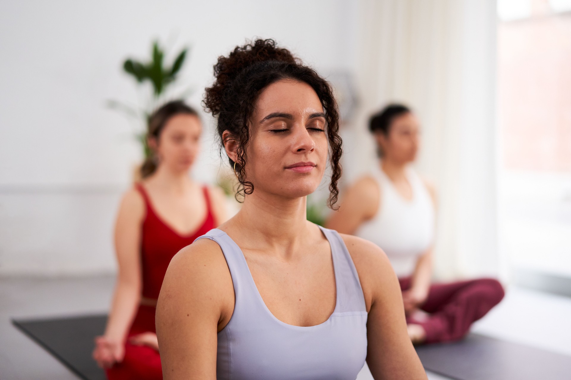 Female yoga trainer guiding a group of women to meditate in lotus position inside studio.